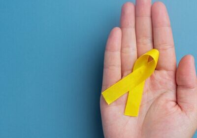 Hands holding yellow ribbon, symbol of cancer awareness, medical support and prevention with helping hand. Suicide prevention day concept