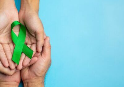 World Mental Health Day; green ribbon put in human's hands on blue background